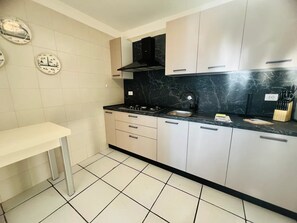 A kitchen with white cabinets, a black countertop, and a tiled floor. - New Listing (Sanremo)