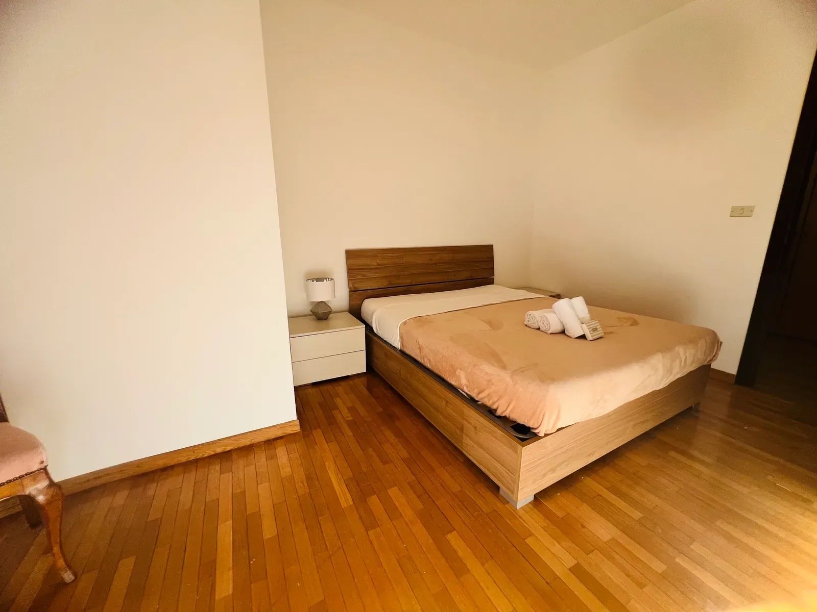 A single bed with a wooden headboard, a bedside table with a lamp, and a chair.
