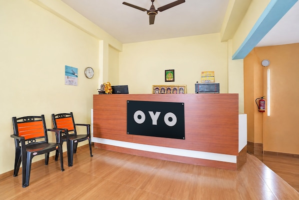 A reception desk with a sign reading 'OYO' in a hotel lobby with wooden flooring and two chairs.