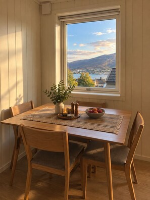 A dining area with a table set for four, a window with a view of a lake and mountains, and a plant on the windowsill. - Cozy Tromsø Home with Fjord View & Northern Lights (Tromsø)