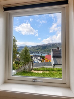 A window with a view of a residential area, including houses and a body of water. - Cozy Tromsø Home with Fjord View & Northern Lights (Tromsø)