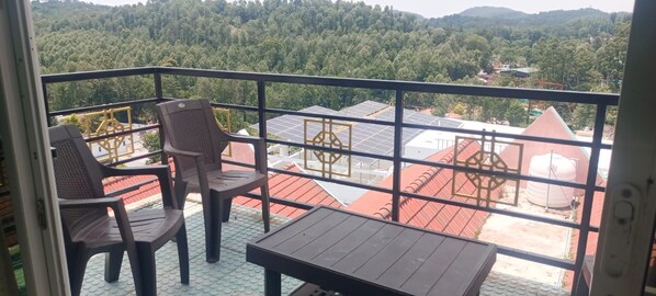 A balcony with two chairs and a table, overlooking a forested area with buildings in the background.