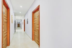Un pasillo con puertas de madera, letreros numerados y piso de baldosas.