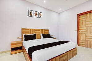 A bedroom with a wooden headboard, a bed with black and white bedding, a nightstand, a phone, and a wooden wardrobe. - Hotel O Naveen Stay (Gurugram)