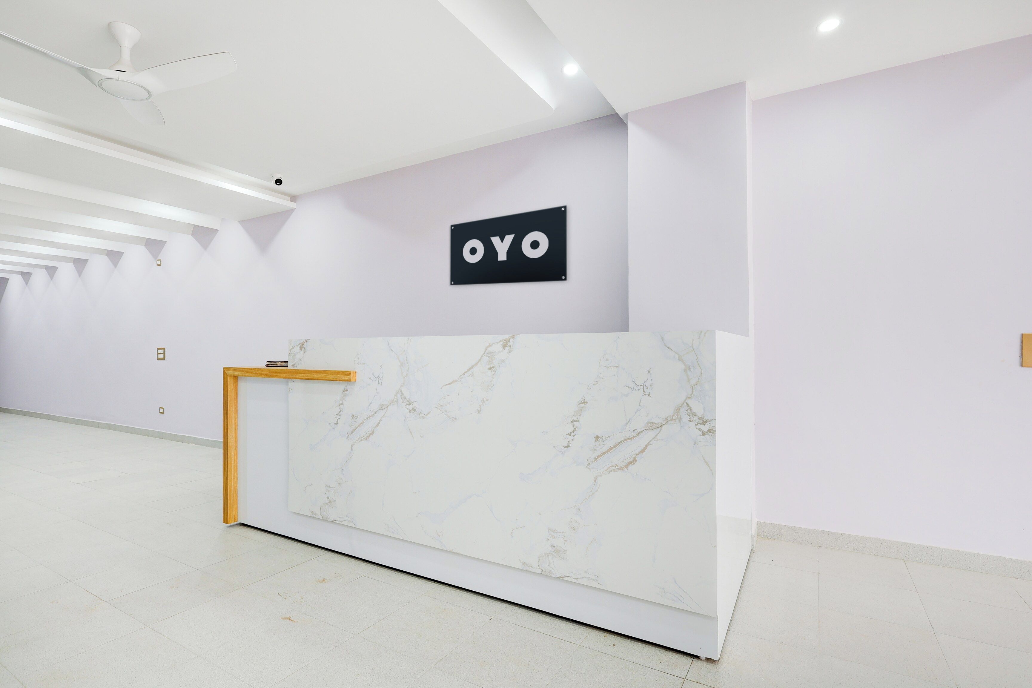 Un mostrador de recepción con encimera de mármol, un ventilador de techo y un cartel con las letras 'OYO' en una pared color lila claro.