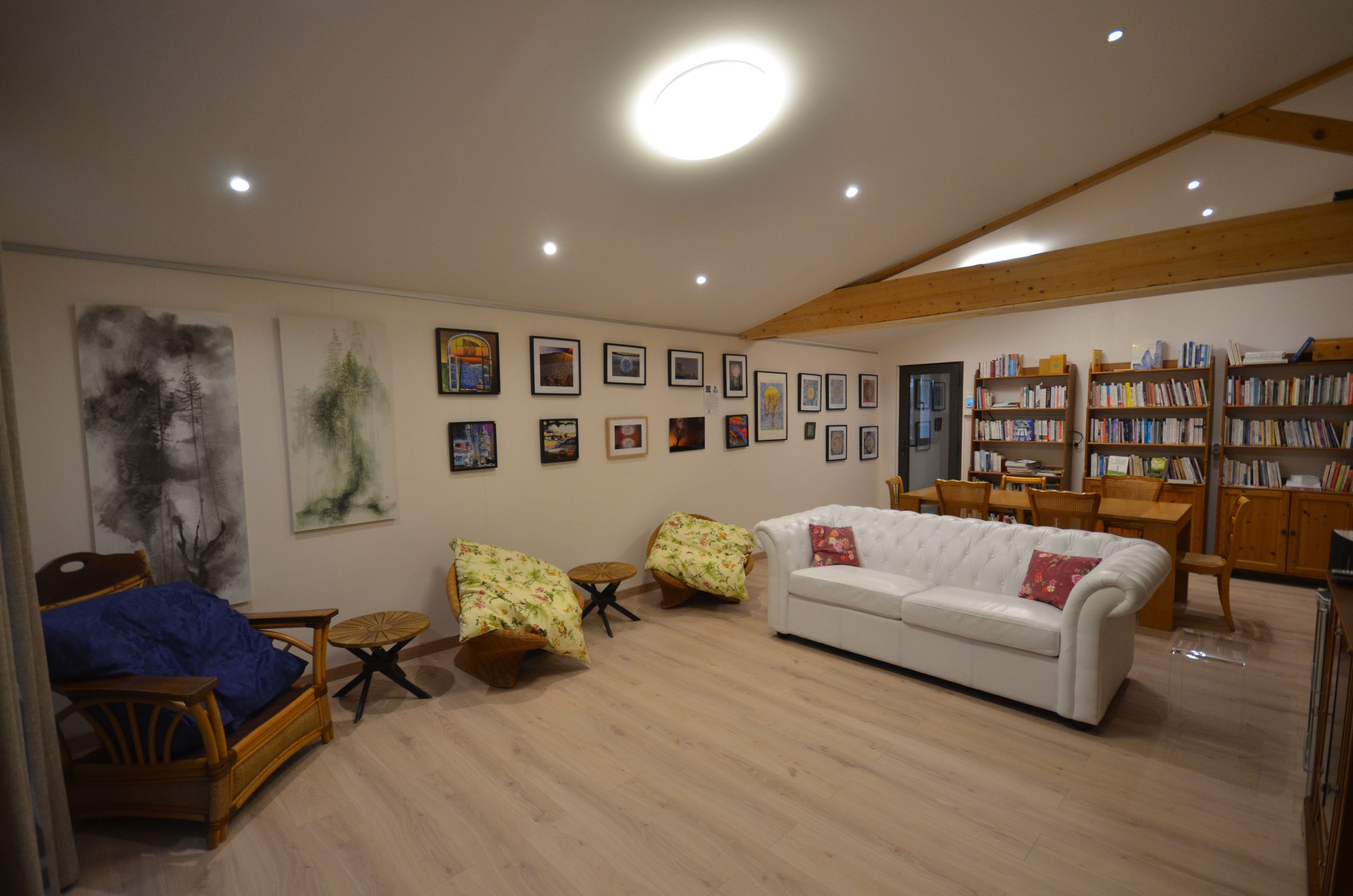 A spacious living room with a white sofa, two armchairs, a coffee table, and a bookshelf filled with books.