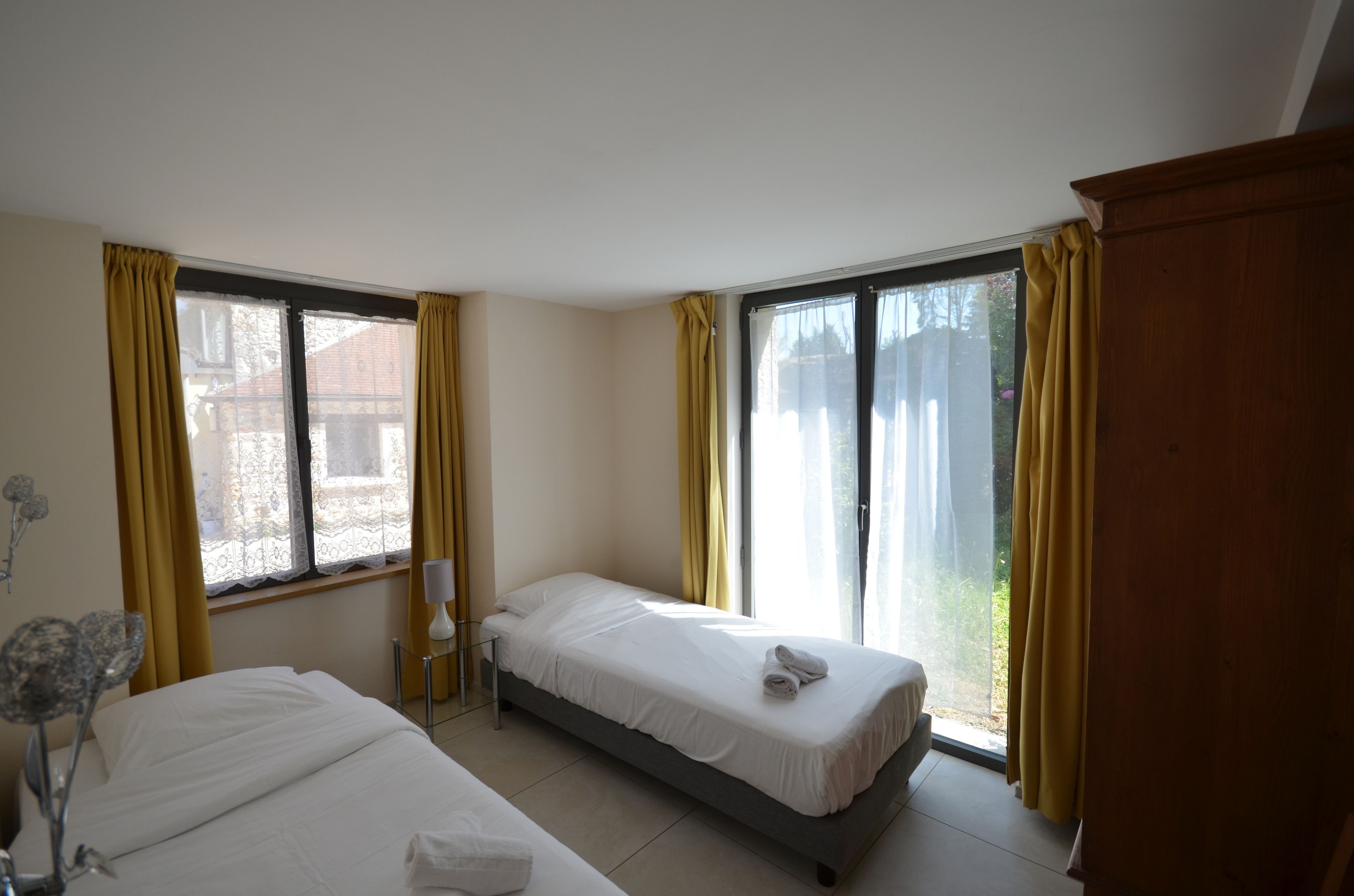 Een hotelkamer met twee enkele bedden, een nachtkastje met een lamp en een groot raam met gordijnen.