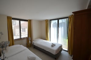 A hotel room with two single beds, a bedside table with a lamp, and a large window with curtains. - Holiday Home 'L'aile Ouest De La Ferme' with Wi-Fi and Air Conditioning (Senlisse)
