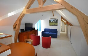 Een moderne loft slaapkamer met een schuine plafond, een televisie, een bank en een rode stoel.