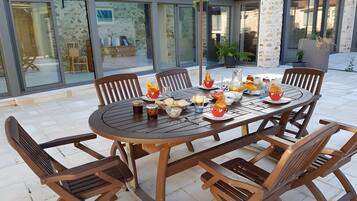 Een terras met een ronde tafel, stoelen en diverse gerechten en drankjes.