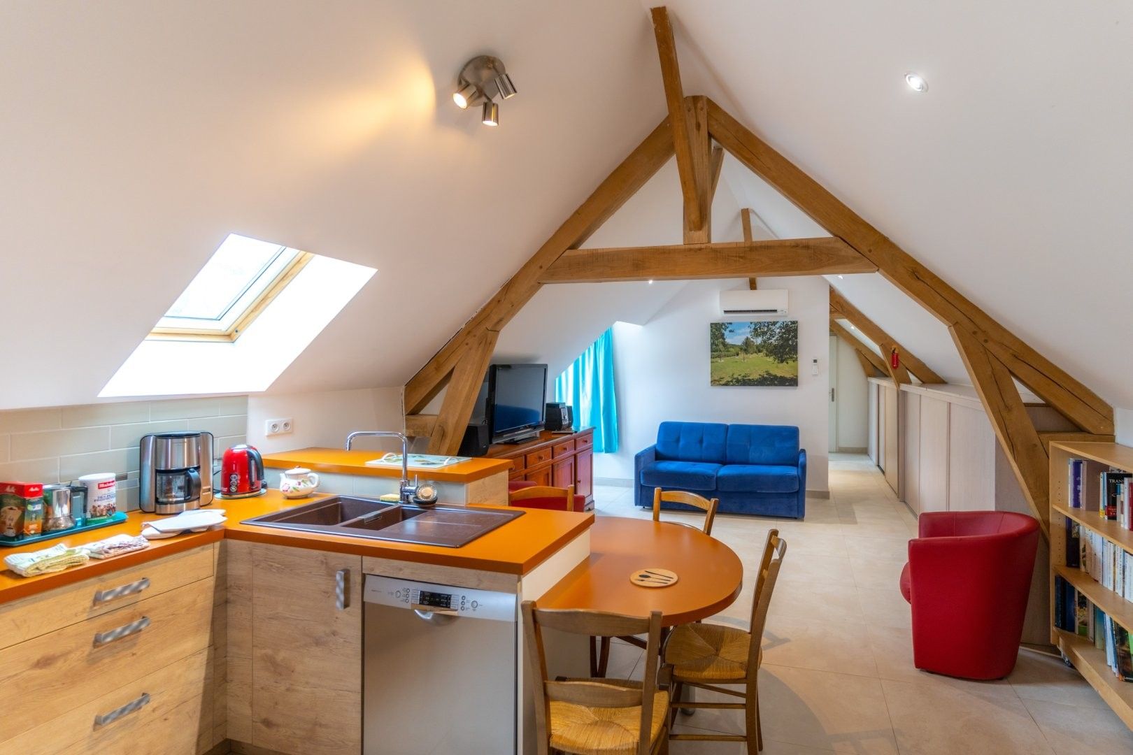 Une cuisine moderne avec un plafond en bois, un coin repas avec une table et des chaises, un pouf rouge et une bibliothèque.