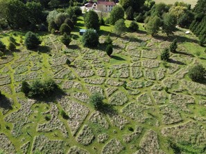 Luchtbeeld van een perceel met een groot, open gazon met geometrische patronen, omringd door bomen en een gebouw op de achtergrond.