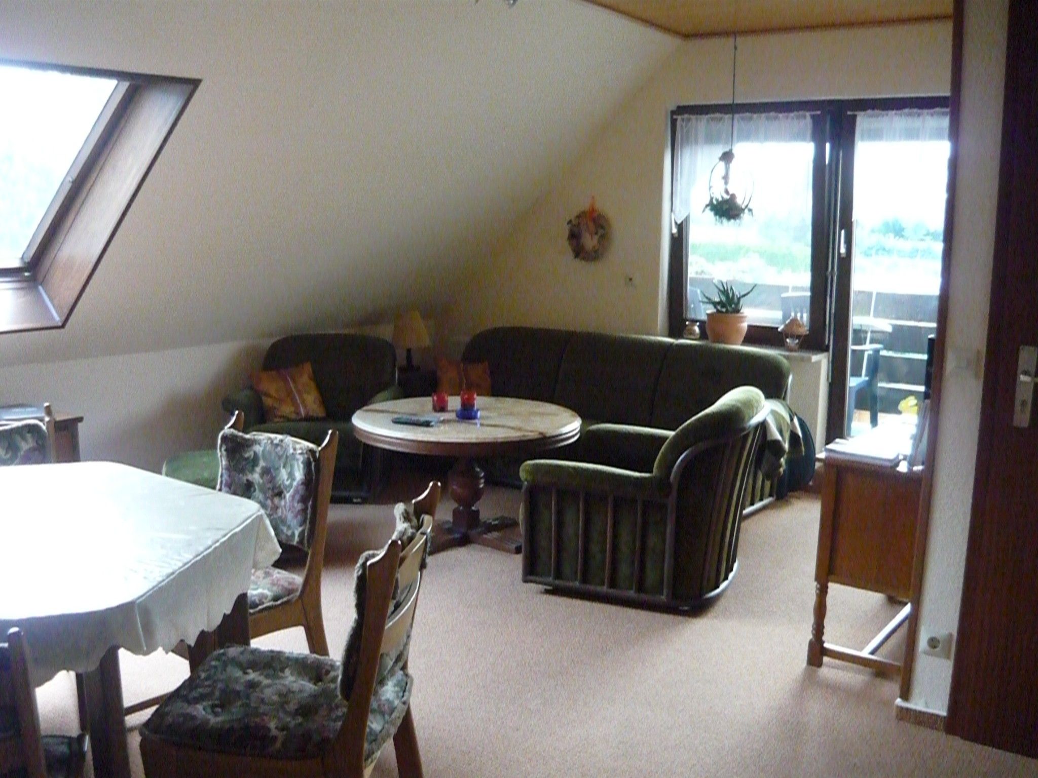 Quarto com mesa redonda, sofá e mesa de jantar com cadeiras. Há uma janela com vista para o exterior.