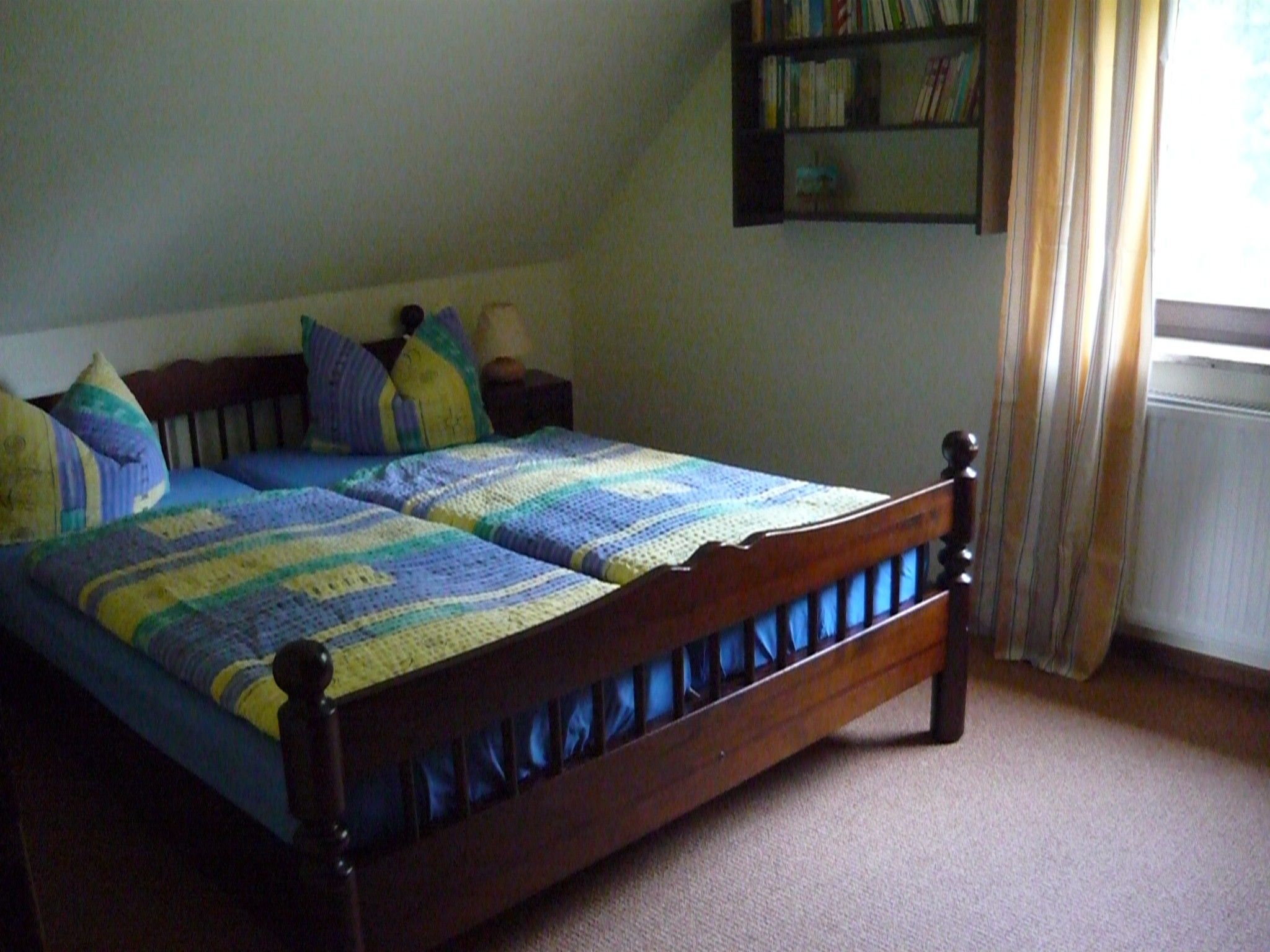 A bed with a wooden frame and a blue and yellow quilt.