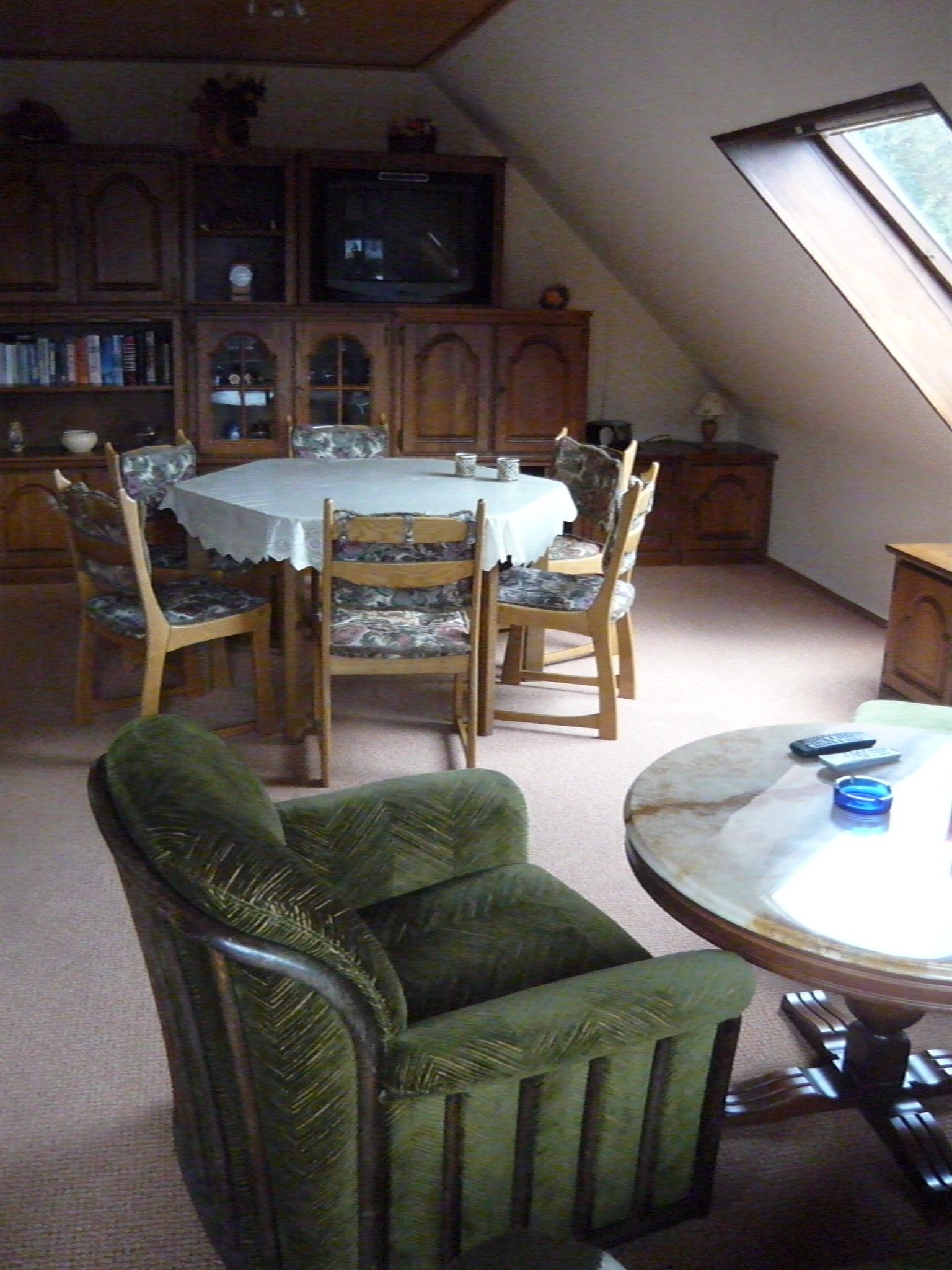 A dining area with a table and chairs, a television in the background, and a window providing natural light.
