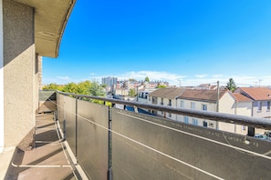 Un balcon donnant sur un quartier résidentiel, avec des maisons et un ensemble d’immeubles plus éloignés.
