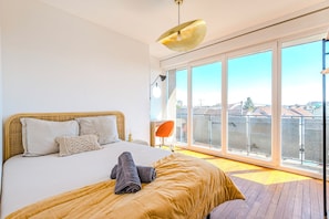 Una camera da letto con un letto grande, vista sulla città grazie a finestre a tutta altezza e un balcone con ringhiera.