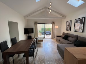 Een moderne woonkamer met een eethoek, een bank, een televisie en een plafondlamp.