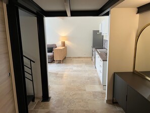Een moderne keuken met een inbouwoven, een koelkast en een spoelbak. Achterin staat een kleine tafel met een lamp en een stoel.