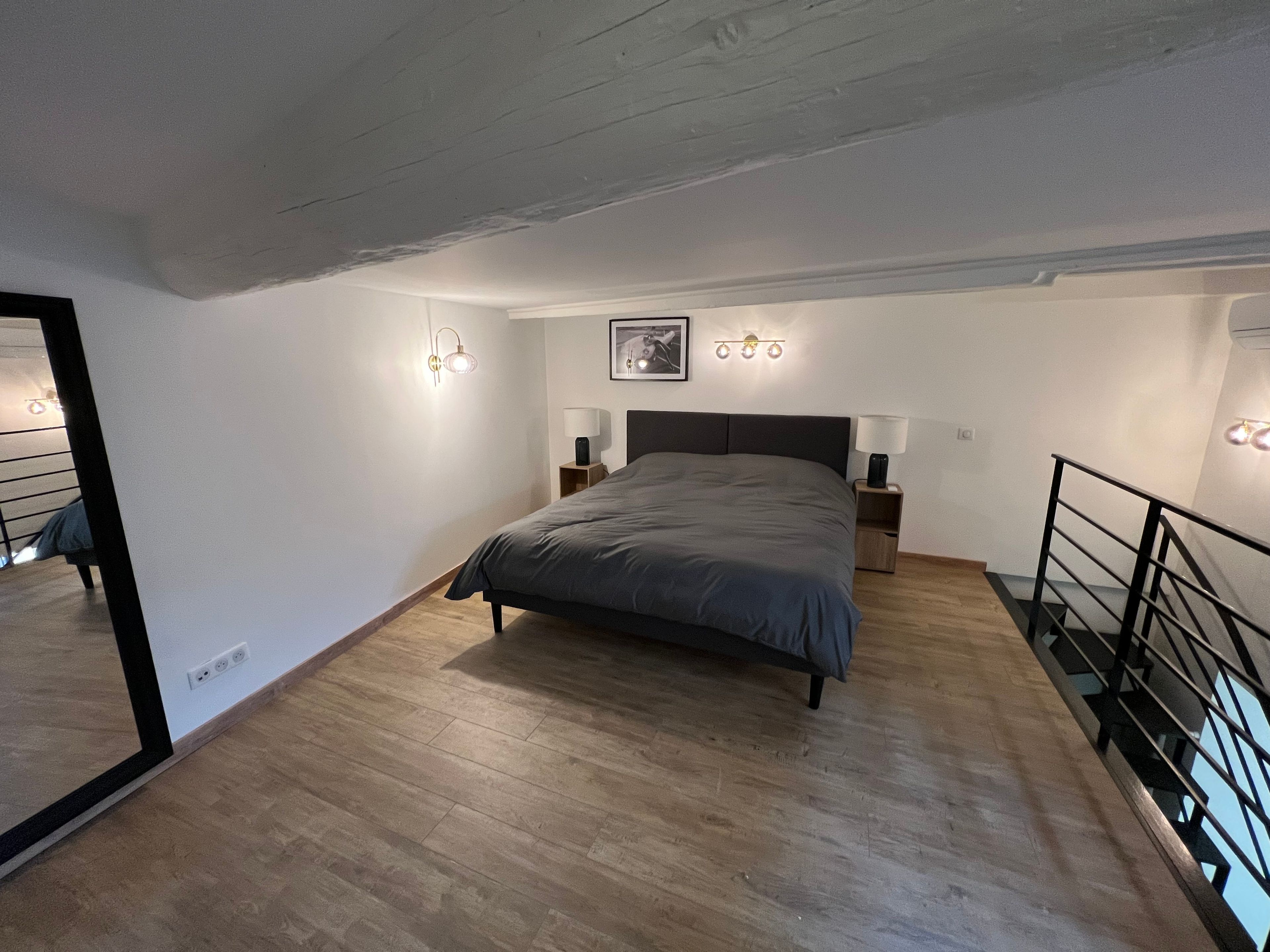 Een slaapkamer met een bed, nachtlampjes, een lijst met een afbeelding en een spiegel.