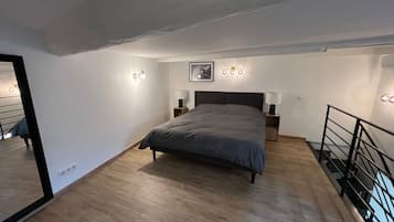 Een slaapkamer met een bed, nachtlampjes, een lijst met een afbeelding en een spiegel.