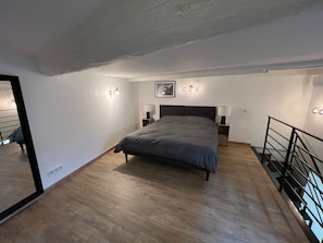 Een slaapkamer met een bed, nachtlampjes, een lijst met een afbeelding en een spiegel.