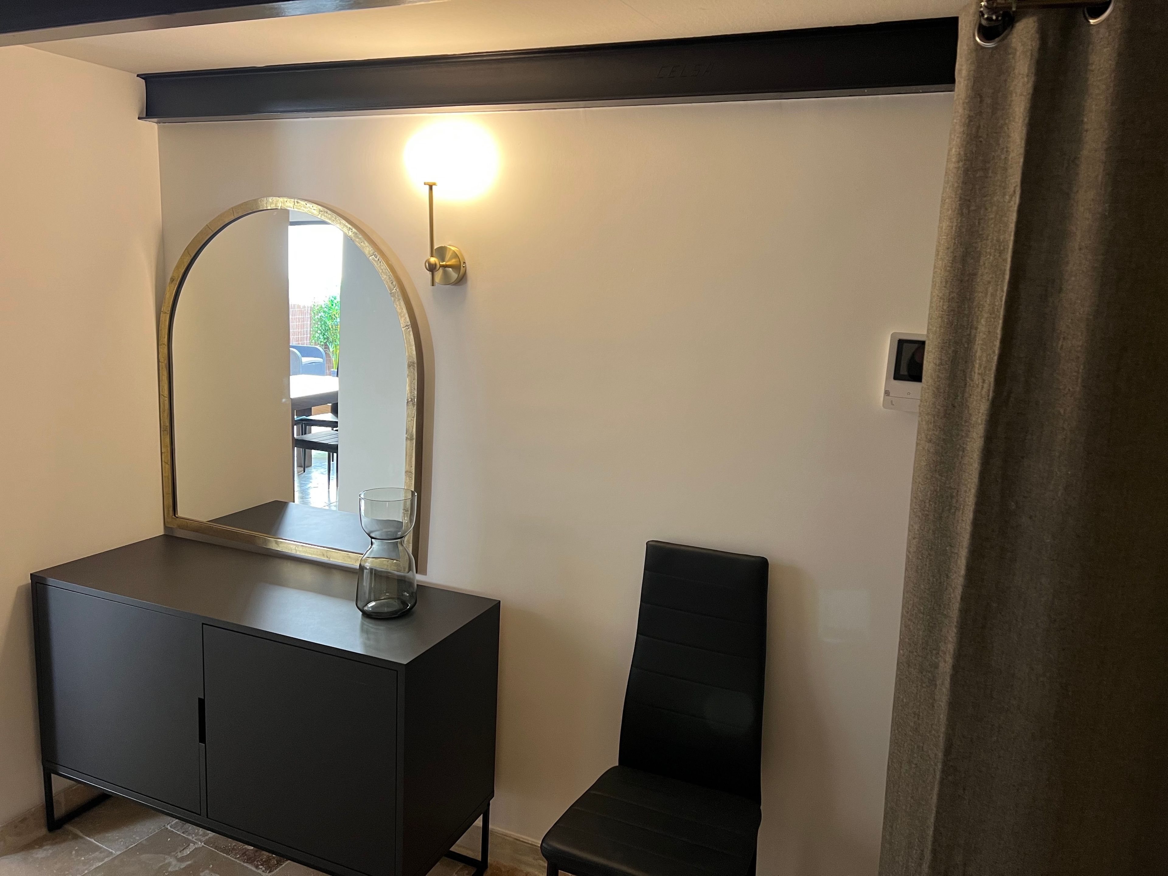 Een badkamer met een zwart wastafelmeubel, een grote spiegel, een wandlamp en een douchegordijn.