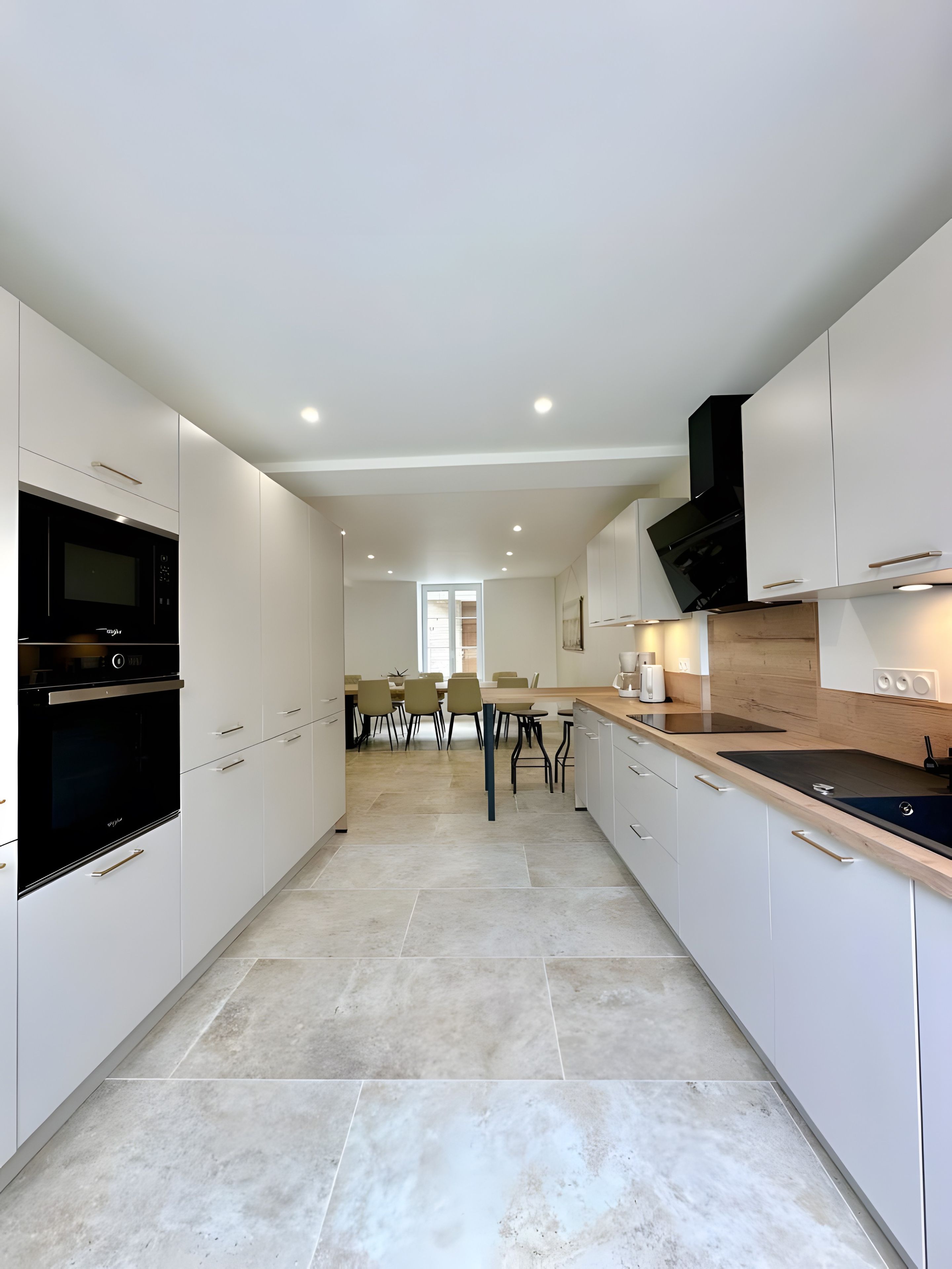 A modern kitchen with white cabinetry, a black oven, and a dining area with chairs and a table.