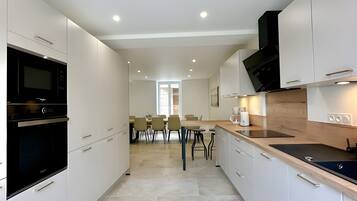 A modern kitchen with white cabinetry, a black oven, and a dining area with chairs and a table.