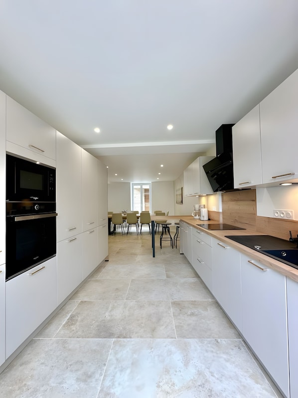 A modern kitchen with white cabinetry, a black oven, and a dining area with chairs and a table. - Holiday Home 'Grand Gîte De Standing 14 Pers' with Private Terrace, Private Garden and Wi-Fi (Alençon)