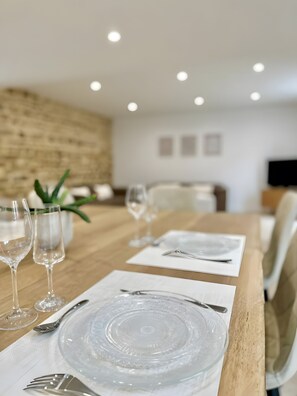 A dining table set with clear glassware and plates, a wooden table, and a brick wall in the background. - Holiday Home 'Grand Gîte De Standing 14 Pers' with Private Terrace, Private Garden and Wi-Fi (Alençon)