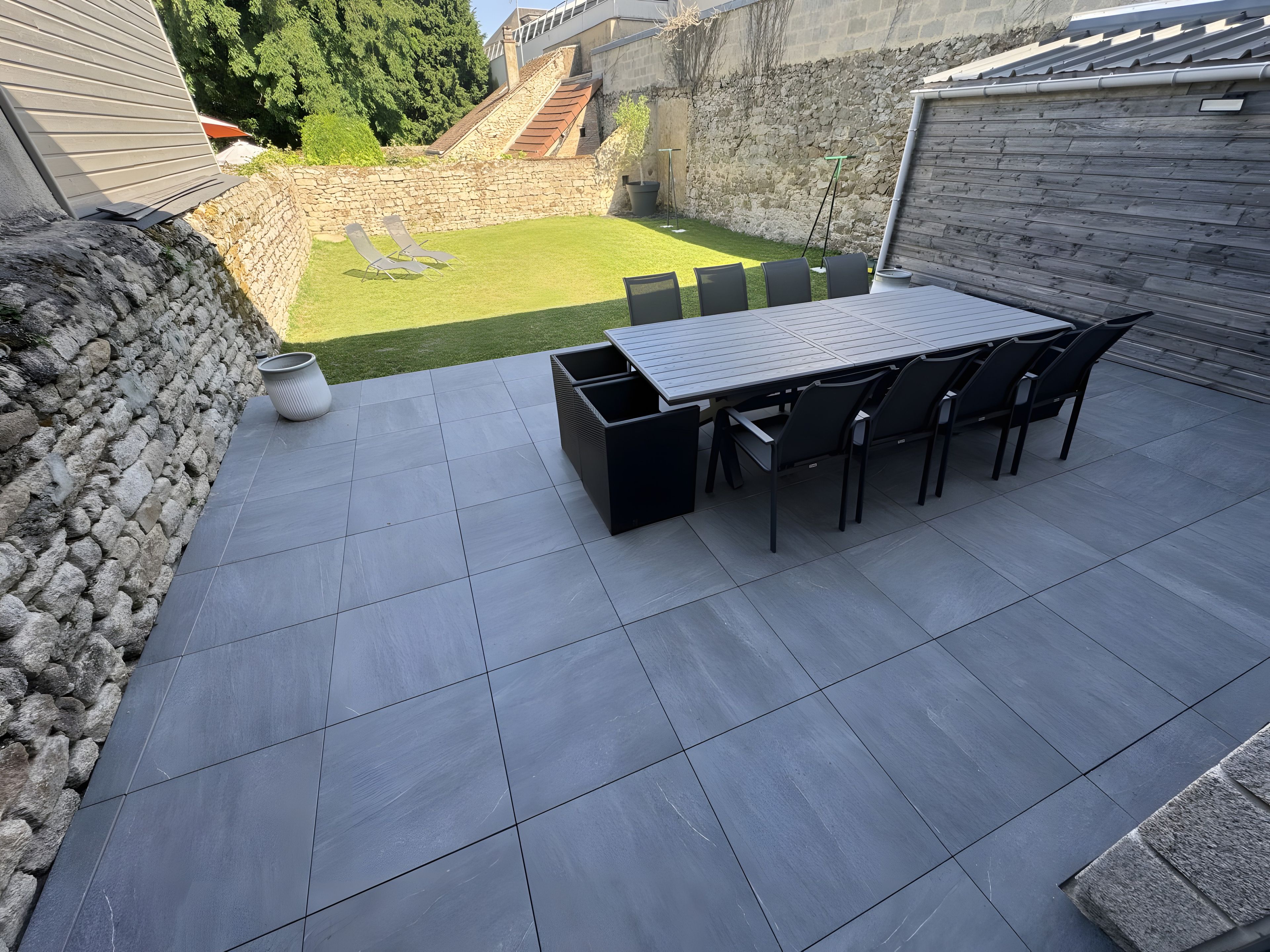 A patio with a table and chairs, a stone wall, and a grassy area in the background.