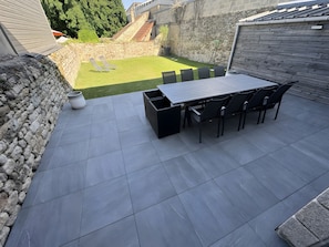 A patio with a table and chairs, a stone wall, and a grassy area in the background. - Holiday Home 'Grand Gîte De Standing 14 Pers' with Private Terrace, Private Garden and Wi-Fi (Alençon)