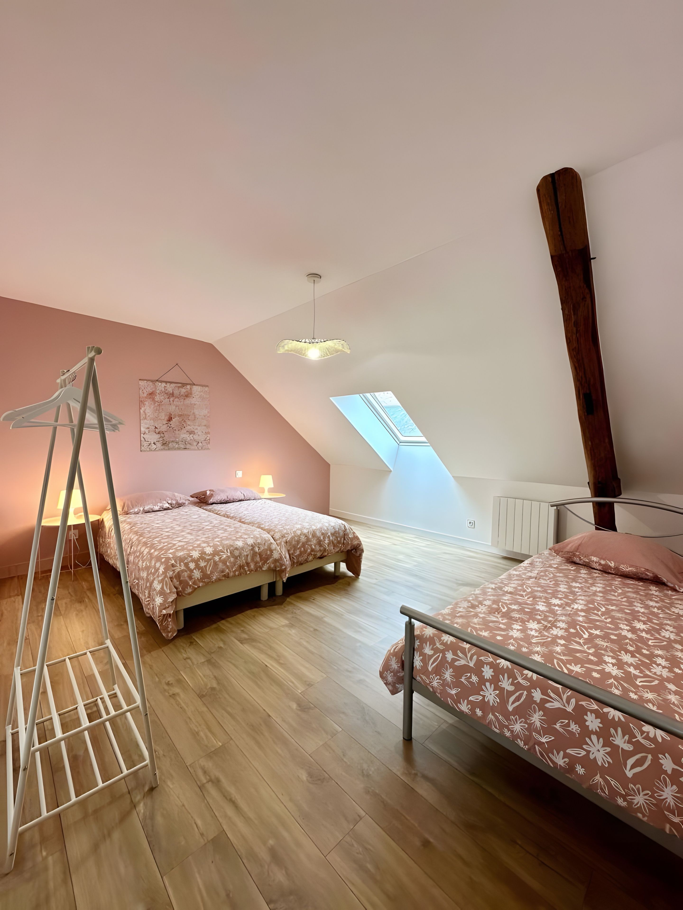 A bedroom with two beds, a wooden floor, a slanted ceiling, and a skylight.