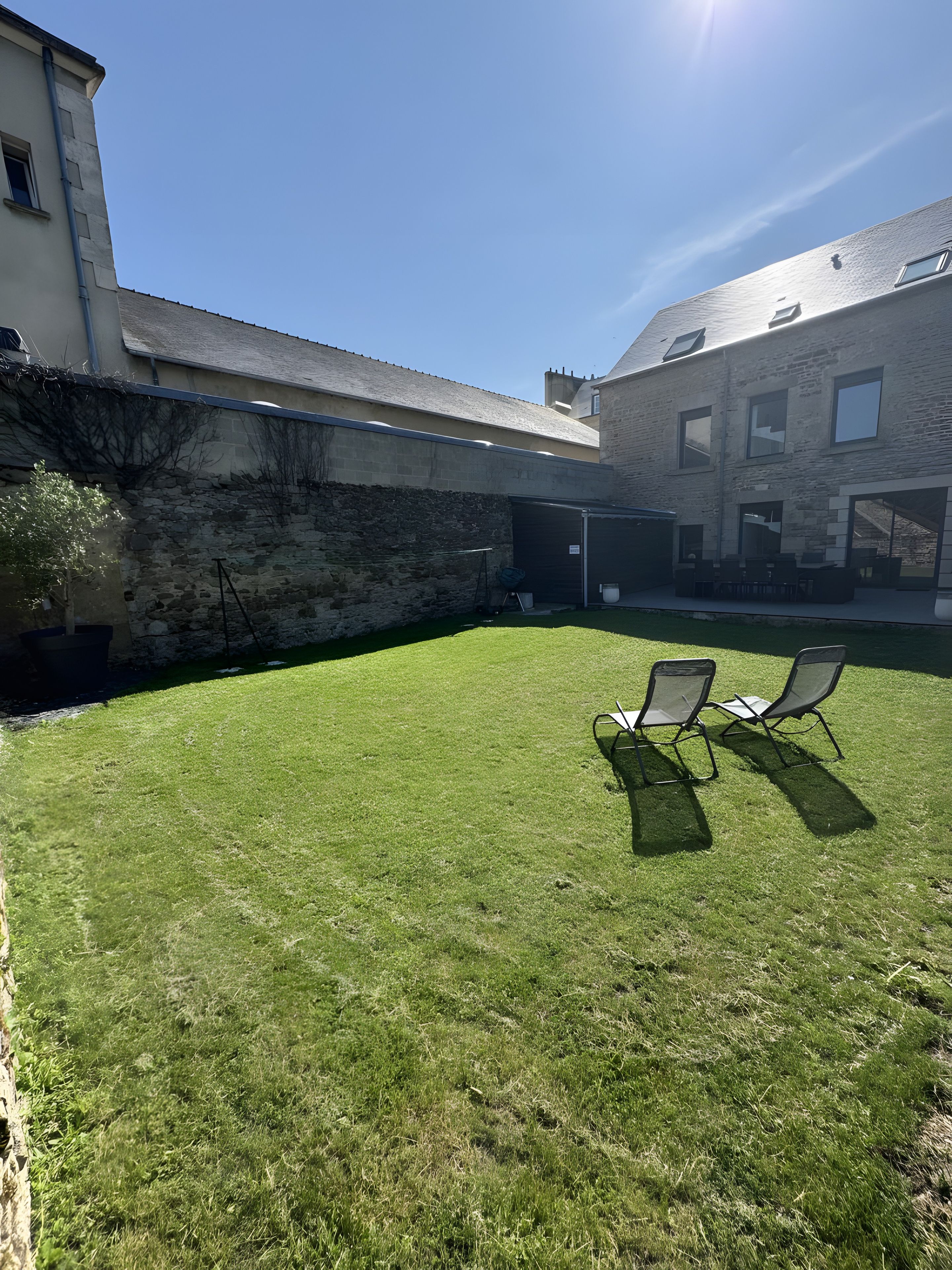 Een verzorgde, gazonrijke achtertuin met een terras en twee comfortabele fauteuils.
