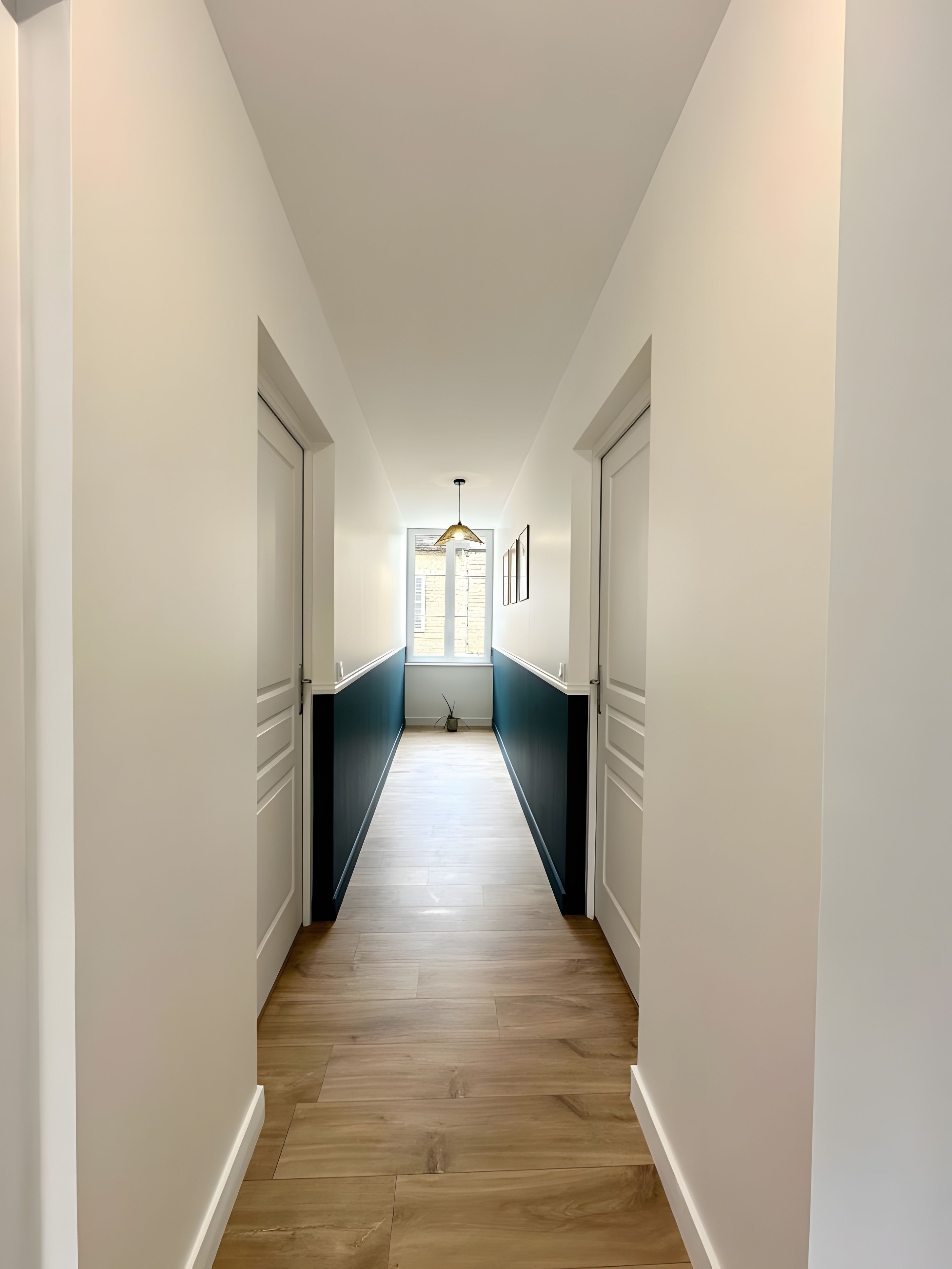 A hallway with a wooden floor, white walls, and a window at the end.