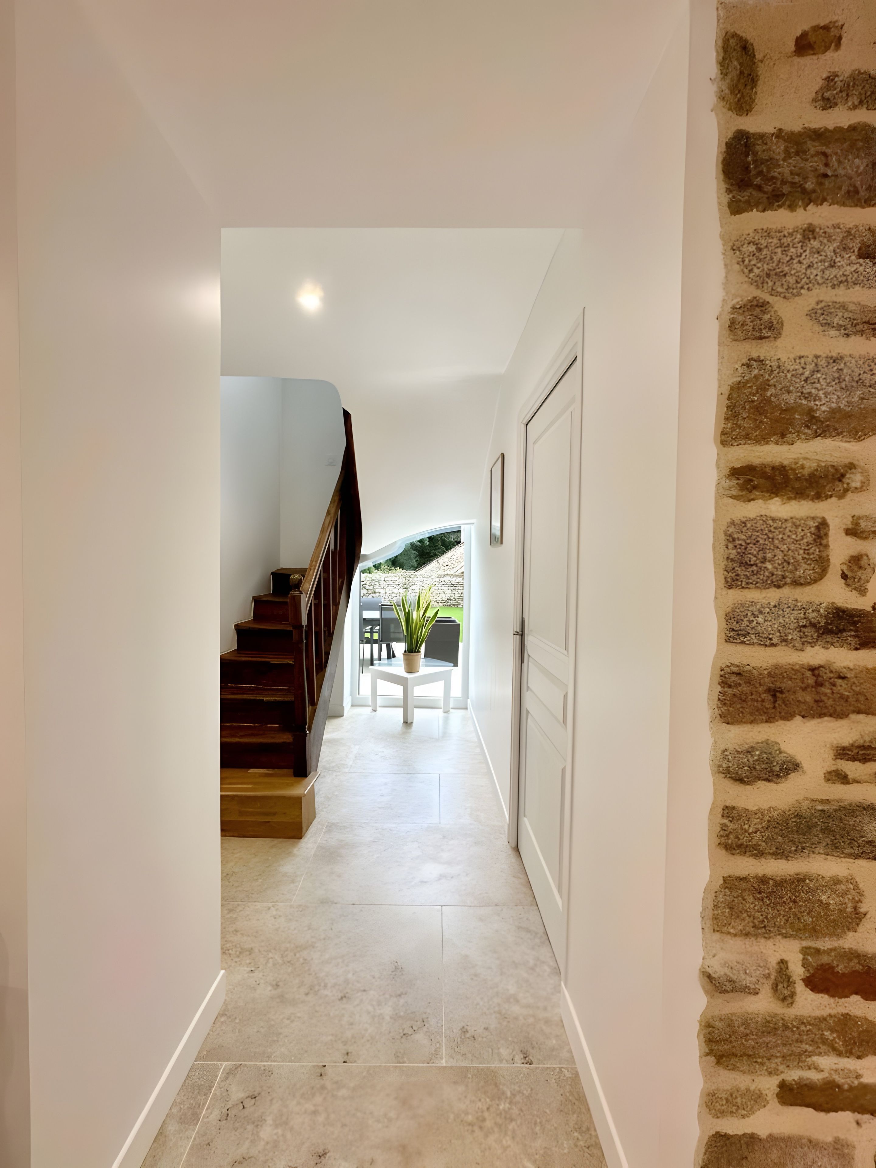 Un couloir avec un escalier, une plante en pot et une porte.