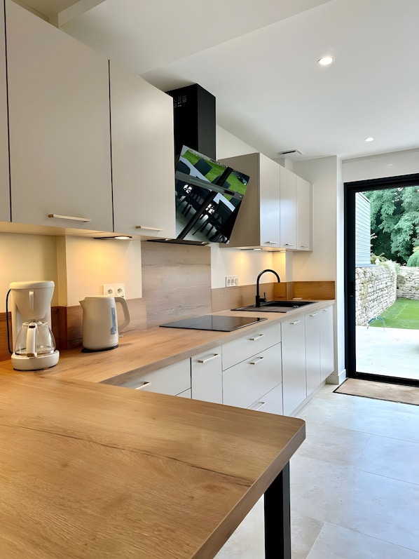 A modern kitchen with a wooden countertop, white cabinets, a built-in oven, and a large window offering a view of the outdoors.