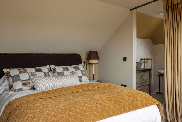 A bedroom with a bed, pillows, a lamp, and a bathroom visible through an open door.