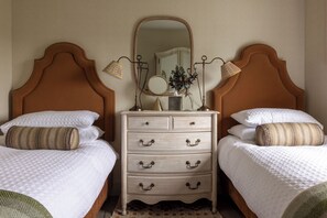 Une chambre avec deux lits, une commode avec des tiroirs, un miroir et deux lampes fixées au mur.
