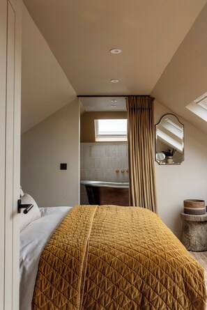 A bedroom with a bed, a window, a mirror, and a small wooden stool.