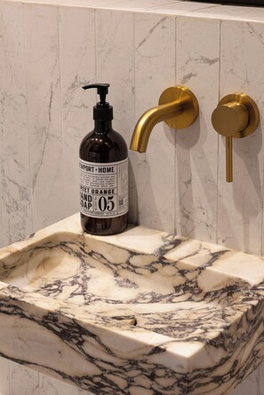 Un lavabo de salle de bain avec un receveur en marbre, un flacon de savon liquide et un robinet doré.