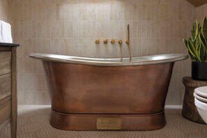 A bathtub with a copper finish, a wooden cabinet, a potted plant, and a toilet.