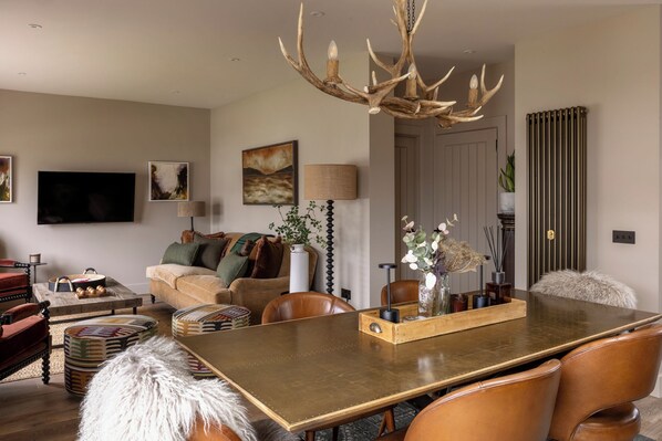 Un salon moderne doté d’une grande table à manger, de fauteuils en cuir, d’une cheminée et d’un lustre original en forme de bois de cerf.