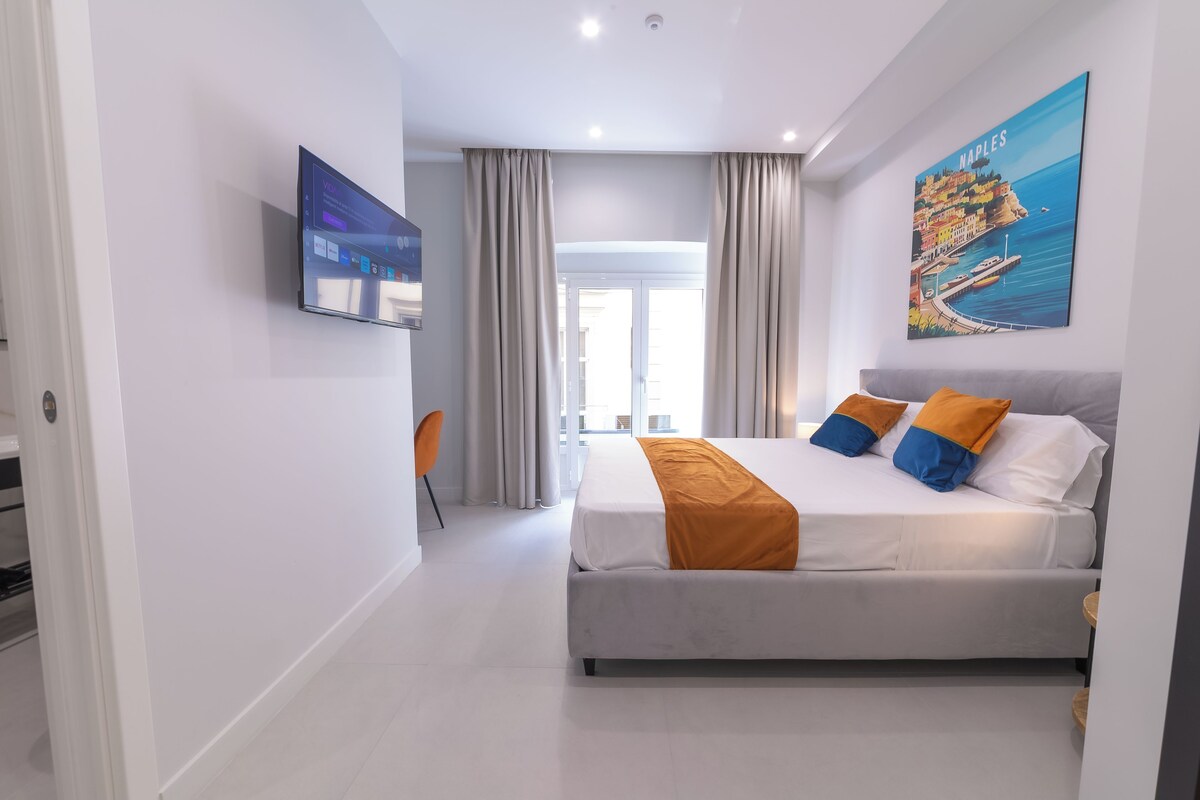 Een moderne hotelkamer met een bed, een televisie en een schilderij van Napels.