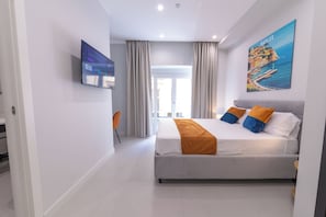 Een moderne hotelkamer met een bed, een televisie en een schilderij van Napels.