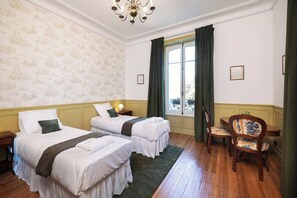 Une chambre d’hôtel avec deux lits, un plancher en bois, une chaise et une fenêtre avec des rideaux.