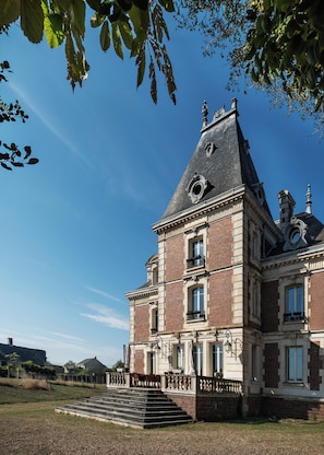 Un edificio grande e histórico con una torre destacada, una imponente escalera y un césped bien cuidado.