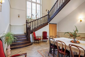 Un comedor espacioso con techo alto, una escalera de madera y vistas al exterior a través de amplias ventanas.
