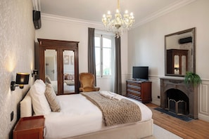 Un dormitorio con una cama grande, televisor, chimenea y espejo.